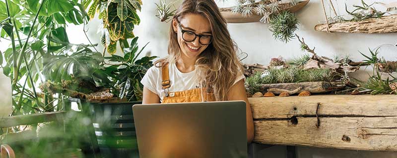 Happy young woman using laptop in a small gardening shop
