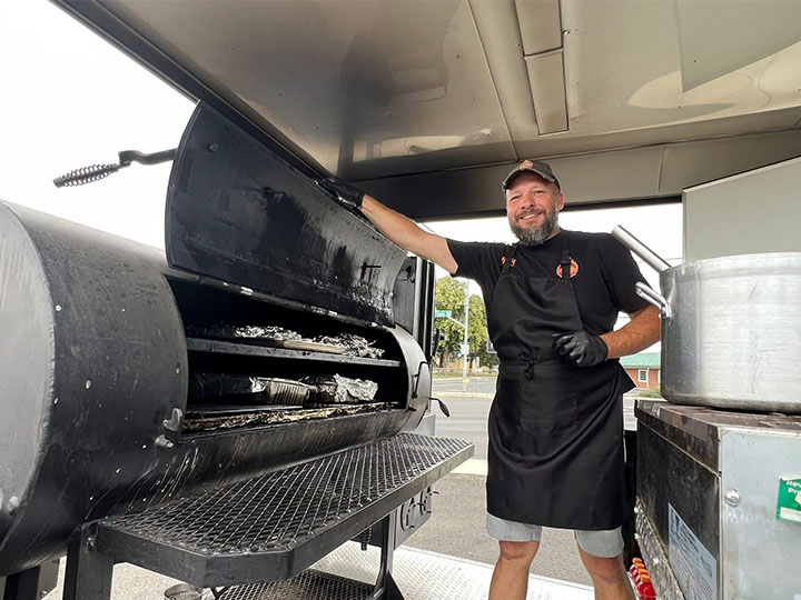 Photo of business owner Rich Anderson in front of a BBQ smoker